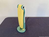 Lamp folded upright showing side profile in green and yellow plastic on dark surface against white background