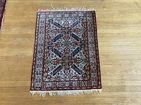 Full view of the rectangular silk mat with Persian traditional patterns on a wooden floor.