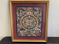 Full view of framed Tibetan Thangka painting with gold frame and red matting, showing entire mandala design.