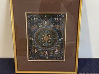 Full view of the framed Tibetan Thangka painting with gold frame and brown matte.