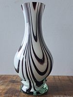 Front view of black and white swirl art glass vase on wooden surface.