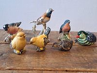 Front view of all 7 bird figurines arranged on wood surface showing various colors and styles.