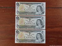 Front side of three 1973 Canadian one dollar bills showing Queen Elizabeth II portrait and consecutive serial numbers BF01586858, BF01586859, BF01586860.