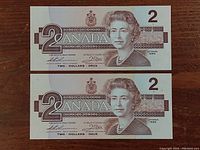 Front view of the two Canadian two dollar bills showing Queen Elizabeth II and denomination details.