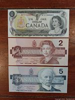Front side of three Canadian bills: 1973 one dollar, 1986 two dollar, 1986 five dollar, each showing portraits of notable figures and Queen Elizabeth II.