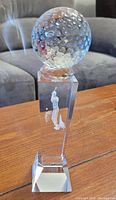 Crystal golf trophy on wooden table, featuring dimpled golf ball and etched golfer figure.