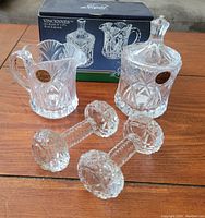 Photo showing crystal cream and sugar set with original box and two crystal cutting utensil rests on wooden table.