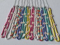Photo of 12 daisy chain necklaces laid flat showing various colors of beads including pink, white, blue, green, yellow, and multi-colored with white beaded flowers spaced on a metal chain