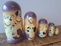 Five hand painted Dalmatian stacking dolls arranged in size order showing detailed dog illustrations and gradient purple to beige coloring.