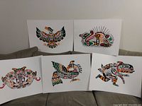 Five First Nations art prints in traditional style by John Nelson showing Eagle, Thunderbird, Sea Monster, Sea Otter and Longhouse Mask on white mat boards.