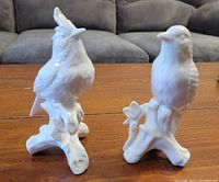 Photo of two white porcelain Godinger bird figurines, each about 5.5 inches tall, on a wooden surface with a couch in the background.