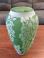 Front view of the tall green and white decorative glass vase showing detailed floral patterns.