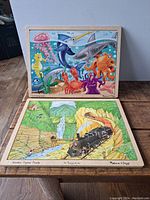 Two wooden puzzles stacked showing the completed images, one train themed and one under the sea themed.
