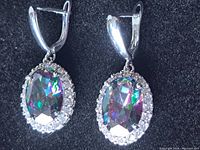 Close-up of the pair of drop earrings with large oval mystic topaz stones and lever-back clasp against a black background.