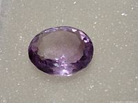 Close-up of oval cut natural amethyst gemstone showing clarity, cut, and purple color.