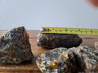 Four raw amber chunks shown on wooden surface, with tape measure for scale on one piece approximately 4 inches long.