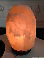 Salt lamp glowing with amber light on stove burner background showing illuminated salt crystal texture.
