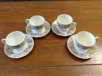 Four floral teacups with corresponding saucers arranged on a wooden surface, showing all pieces in the set.