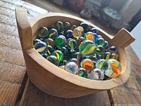Wooden bowl filled with various colorful glass marbles, showing different sizes and designs