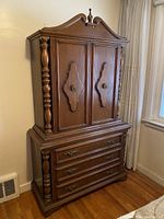 Wooden traditional style armoire with ornate carved details and three drawers at the bottom.