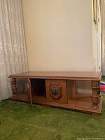 Rectangular wooden coffee table with turned legs and central cabinet under the top surface, placed on green carpet.