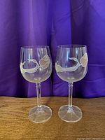 Photo of two clear wine glasses with floral print design on their bowls, shown against a purple fabric backdrop on a wooden surface.