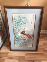 Full view of wood framed and matted bird artwork with blue matting, depicting two birds on a flowering branch with Asian characters. Frame has scratches.
