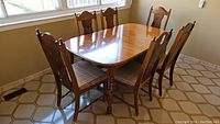 View of all six wooden dining chairs arranged around a table in a room with tiled floor and large windows.