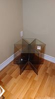 Photo of the vintage plexiglas and glass end table showing the segmented star-shaped base with a glass top, placed against a wall on wood flooring.