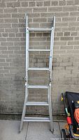 Front view of the aluminum metal extension ladder leaning against a brick wall, showing the intact rungs and extension sections.