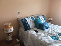 Two bedside lamps with glass and metal elements on nightstands beside a bed with blue and gray bedding.