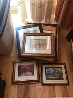 Top view of all six frames, showing four framed prints and two empty frames stacked on wood floor near window.
