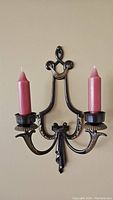 Front view of one metal wall sconce with two pink taper candles mounted on wall.
