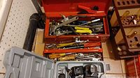 Metal toolboxes filled with assorted hand tools including pliers, screwdrivers, wrenches, and tin snips on tiled basement floor.