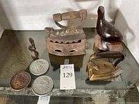 Two antique cast-iron irons, carved wood seal and penguin, and three replica coins displayed on glass table.