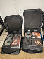 Two open black zippered binders side by side, each filled with stacks of CDs and inserts visible in sleeves