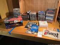Wide view of lot showing stacks of older computer game CDs, assorted game titles visible, box of TDK CD-Rs, spindle of blank discs