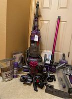 Upright DC15 Ball Multi Floor and V6 MotorHead handheld vacuum with various attachments and cleaning supplies arranged on floor.