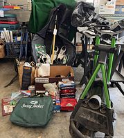 Full overview of two golf travel bags, two push carts, golf shoes, box of golf balls, Swing Jacket tote and assorted accessories on floor