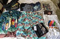Photo showing all items spread out on a bed including multiple graphic T-shirts, two Hawaiian shirts, and a black hoodie