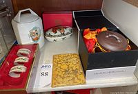Full lot photo showing all items including napkin rings in red tray, white porcelain jar, Mikasa oval box, and Japanese matte glazed box in black box with certificate