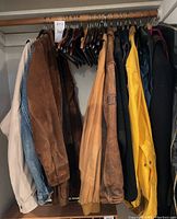 View of assorted jackets and coats on wooden hangers in closet, showing various colors and fabrics.
