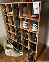 Wooden shoe cubby with multiple pairs of shoes inside each compartment, plus slippers and shoe horns on the floor