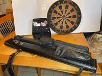 Overall view showing two black vinyl pool cue cases, one open with cues, Dart Master darts case and Pub Master dartboard in background