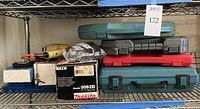 Photo of assorted tool cases and boxes, stacked on a metal rack shelf, containing cordless drills, circular saw, screwdriver sets, and socket sets.