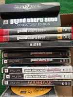 Stack of PS3 games, PSP games and PC game boxes on green cloth.