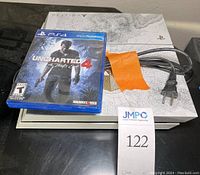 Sony PS4 Destiny Limited Edition console with power and HDMI cables, orange tape securing cables, and Uncharted 4 PS4 game case on top.
