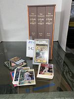 Three Calvin and Hobbes volumes in brown slipcase standing behind graded Barry Bonds card and piles of assorted cards