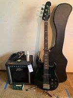 Full view showing bass guitar, amp, gig bag, pedal, tuner, strings and cable