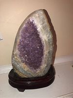 Front view of the amethyst geode on a dark wooden base showing the purple crystal interior and white quartz border.